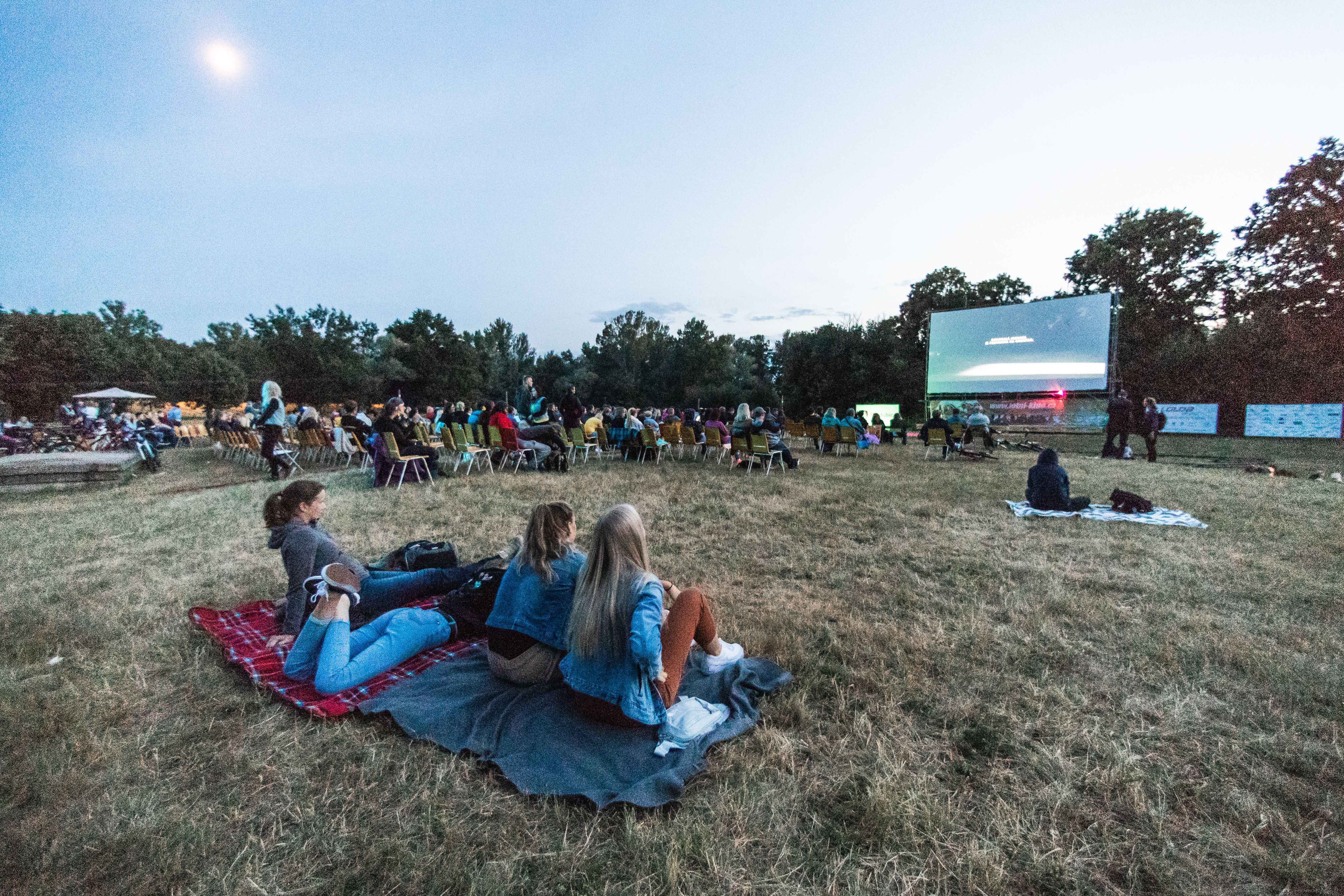 People sitting relaxed on green grass watching an outdoor screen