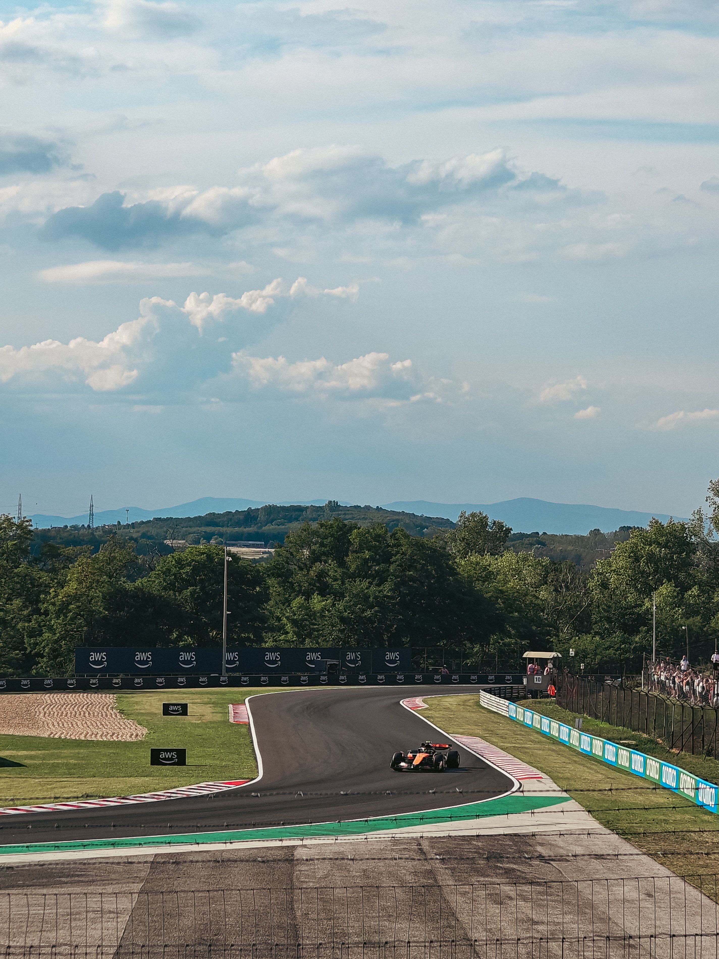 Formula 1 car racing on circuit with spectators and green parkland landscape surrounding the track